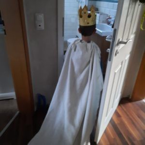 Kind mit Pappkrone und Decke als Umhang steht in offender Tür