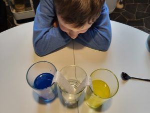 Kind schaut auf drei Gläser mit verschiedenen Flüssigkeiten