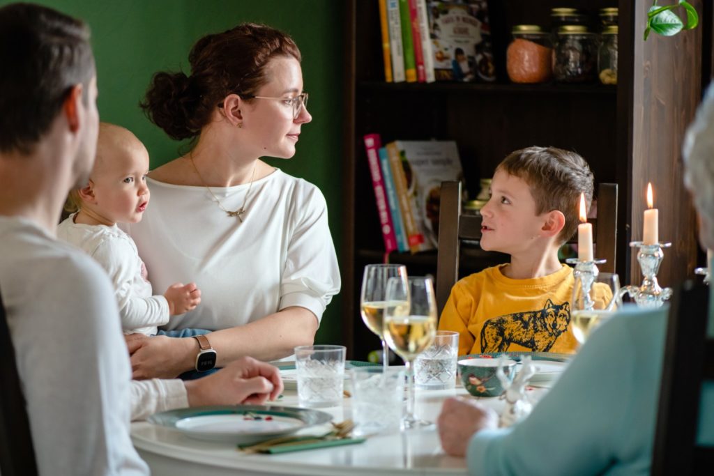 Frau sitzt mit zwei Kindern am Esstisch und unterhält sich mit ihnen