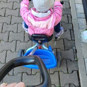 Kind mit pinker Jacke auf blauem Dreirad